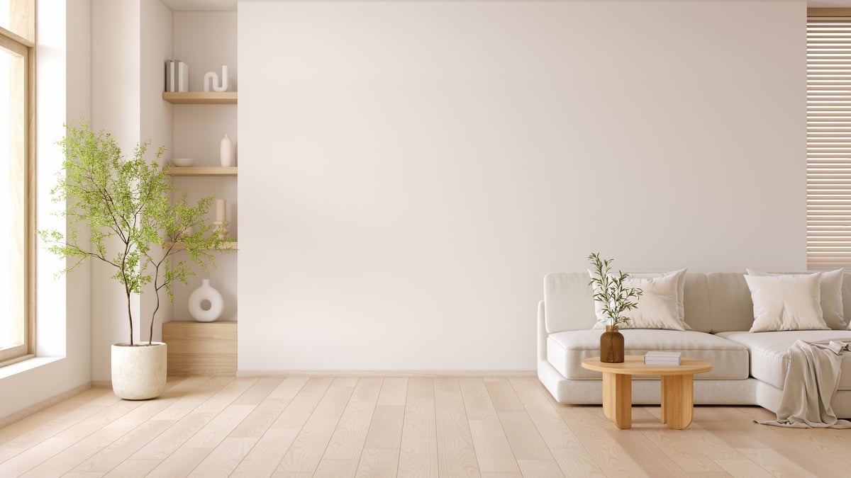 A bright living room with a sofa, a round wooden table and a large bare wall